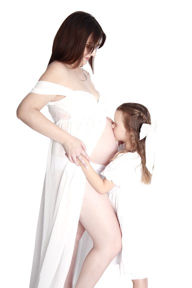 Big sister kissing mothers pregnant belly - maternity photoshoot